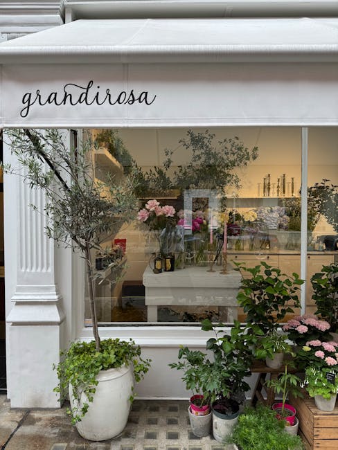The image shows the exterior of grandirose, a floral shop with a large glass window displaying an assortment of fresh flowers and floral arrangements inside, illuminated by warm lighting. Outside, the