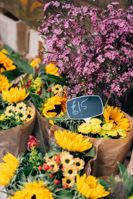 A vibrant display of fresh floral arrangements featuring bright yellow sunflowers with large, daisy-like petals and dark centers, alongside smaller yellow and white chrysanthemums and delicate red and