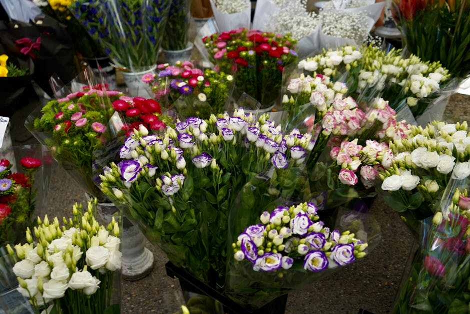 A vibrant display of fresh floral bouquets arranged in a florist shop, featuring a variety of flowers including purple and white irises, pink and white roses, and small pink blossoms. The bouquets are